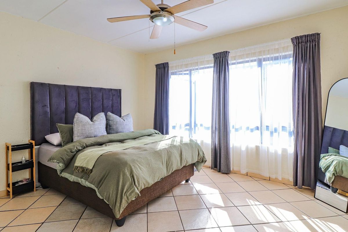 A spacious bedroom featuring tiled flooring, a ceiling fan, and large sliding glass doors that provide ample natural light.