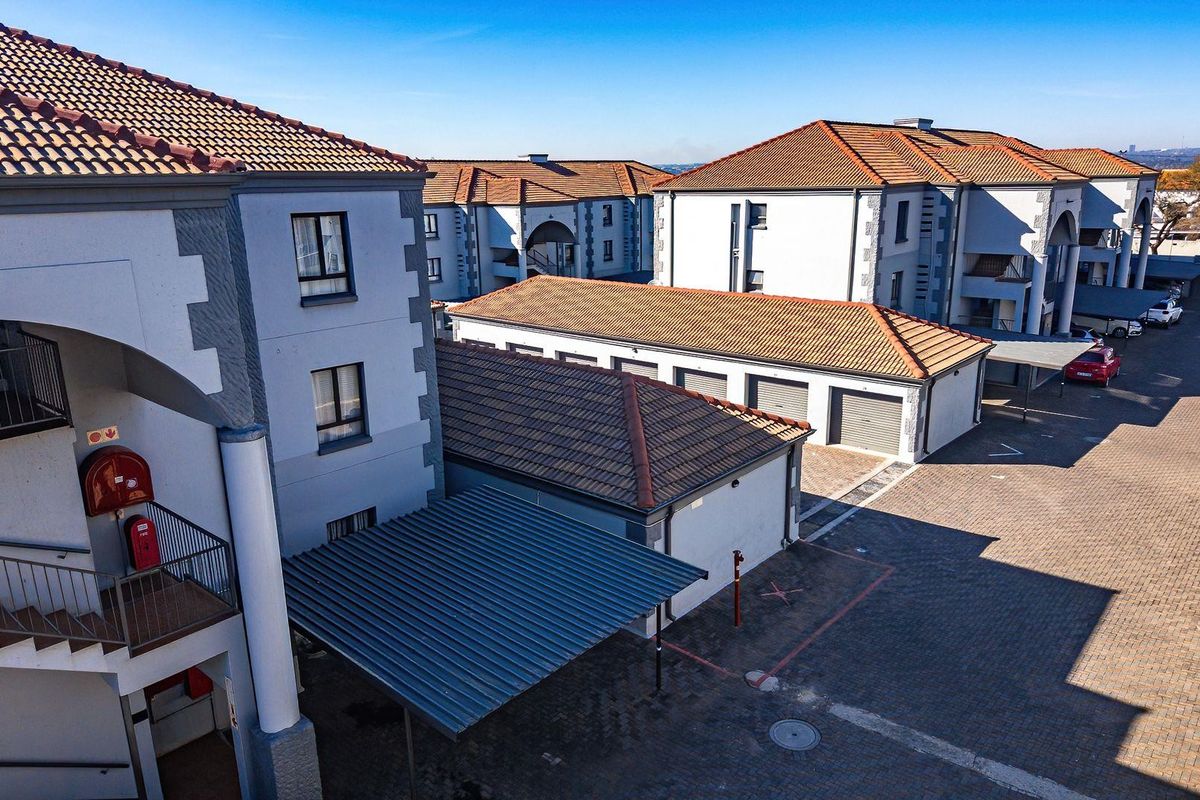 An aerial view of an apartment complex featuring multiple buildings with tiled roofs, paved parking areas, garages, and covered carports.