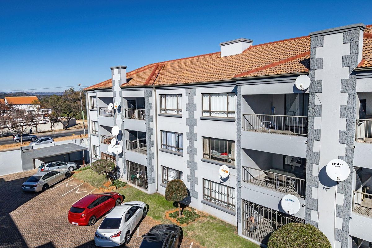 Aerial view of a multi-story apartment complex featuring terracotta tiled roofing, private balconies with metal railings, and a paved parking area.