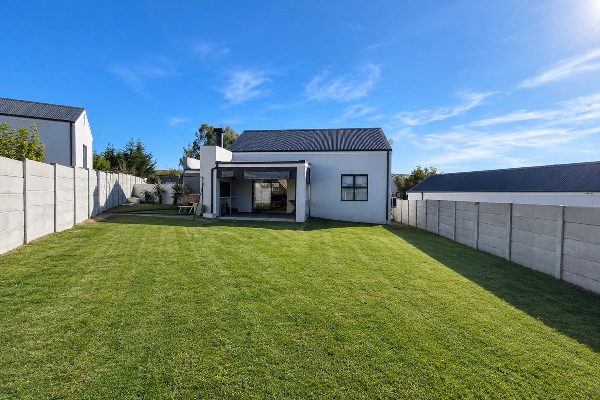 Spacious rear garden featuring a well-maintained lawn, enclosed by precast concrete boundary walls, with a covered patio and outdoor fireplace attached to the home.