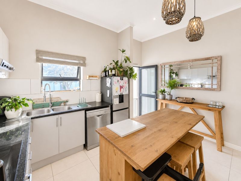Modern kitchen featuring light-toned cabinetry, dark countertops, double basin sink, and tiled flooring, with an integrated dining area and direct outdoor access.