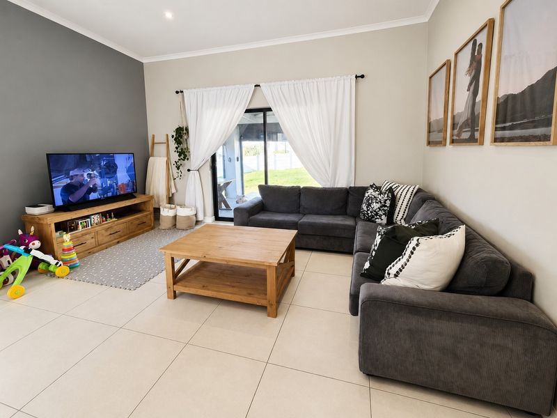 A bright and well-maintained living room featuring large format floor tiles, a feature wall, and sliding glass doors providing access to the outdoor area.