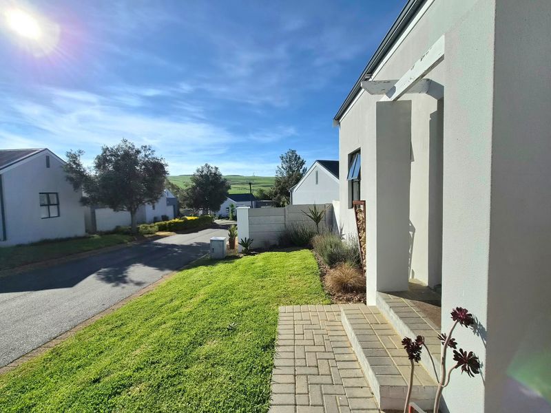 Front exterior view of the townhouse featuring a paved walkway, concrete steps, and a well-maintained lawn with a view of the surrounding estate.