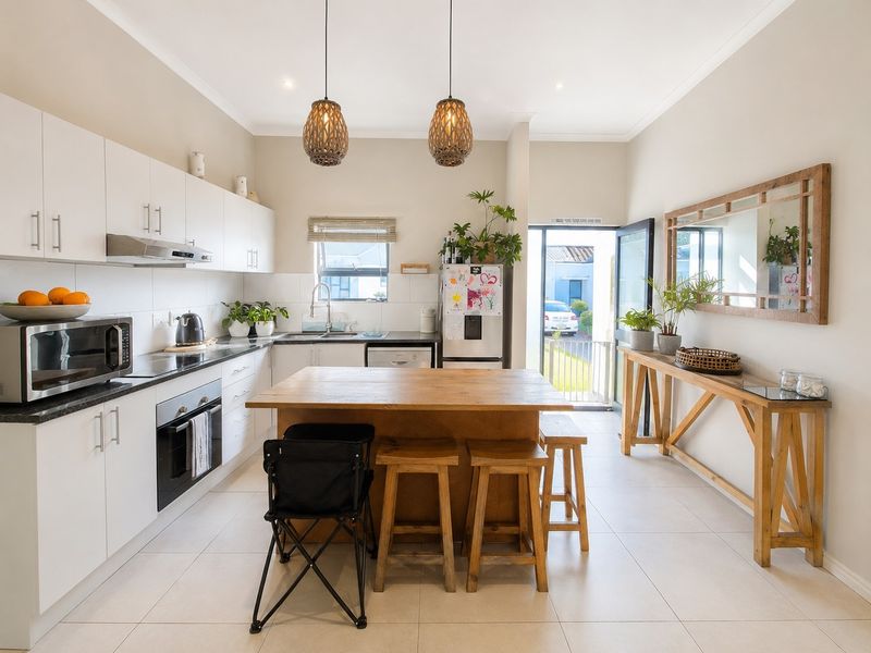 Modern kitchen featuring white cabinetry, dark countertops, integrated oven and hob, and a central wooden island with breakfast seating.
