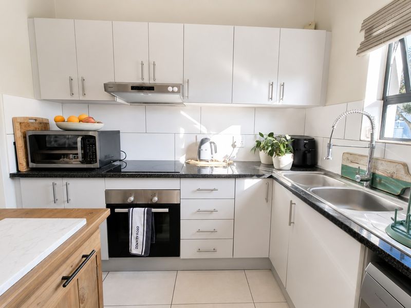 A well-maintained kitchen featuring white cabinetry, granite countertops, a built-in oven, electric hob, and a double bowl sink with a modern gooseneck tap.