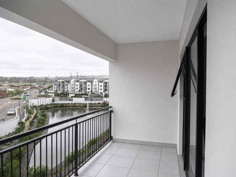 A clean, modern covered balcony featuring tiled flooring and a metal balustrade, offering pleasant views of the surrounding estate and water feature.