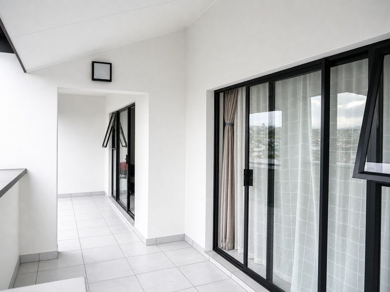 A clean, modern balcony featuring tiled flooring, black aluminium sliding doors, and a neutral white finish, offering a bright and well-maintained outdoor space.