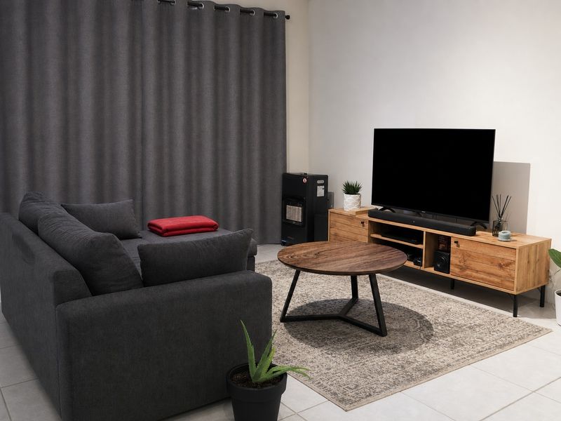 A well-maintained living room featuring neutral tiled flooring and full-length curtains, providing a clean and functional space.