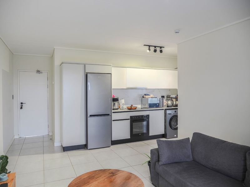 Modern open-plan apartment featuring a compact, well-equipped kitchen with built-in cabinetry, integrated oven, and hob, seamlessly flowing into the living area.