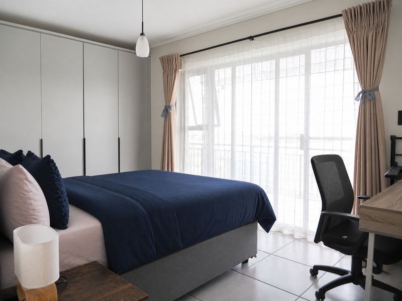 A well-maintained bedroom featuring built-in cupboards, tiled flooring, and a large sliding glass door providing natural light and access to a balcony.