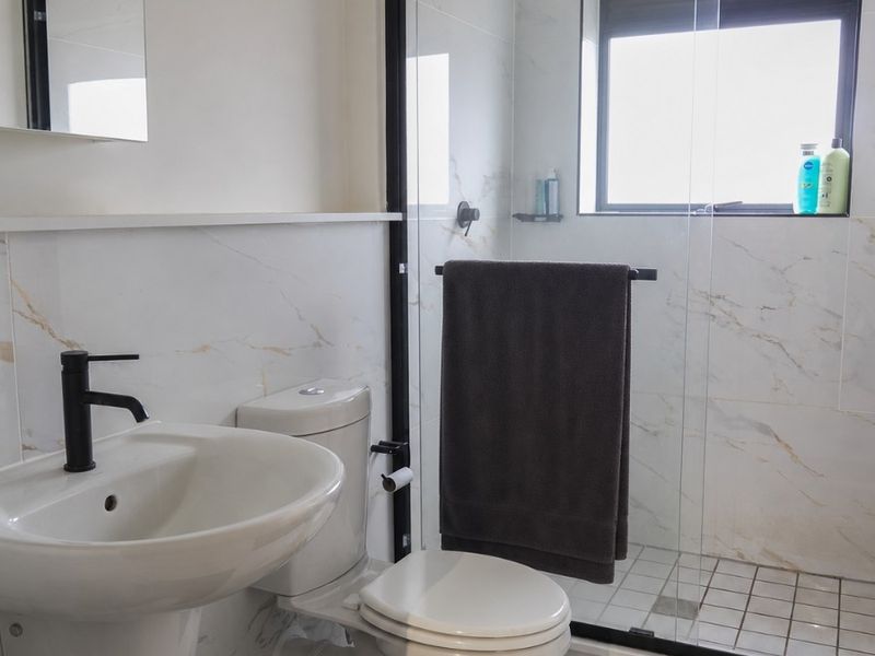 Modern bathroom featuring a pedestal basin with black fixtures, a walk-in shower with a black-framed glass screen, and elegant marble-look wall tiling.