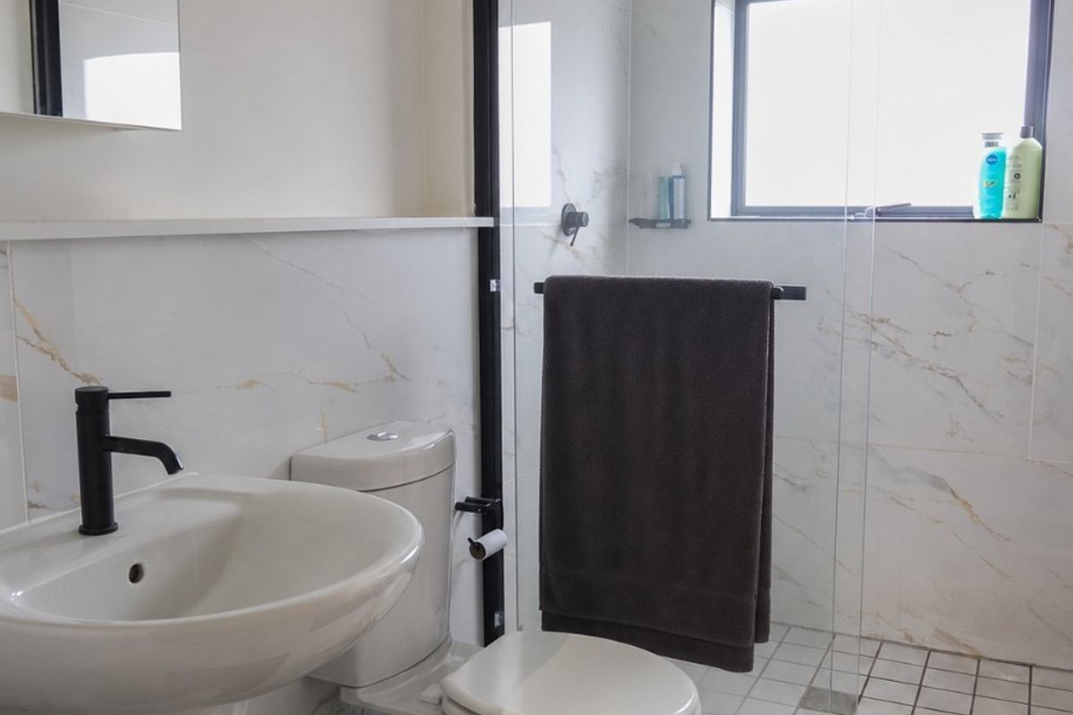 Modern bathroom featuring a pedestal basin with black fixtures, a walk-in shower with a black-framed glass screen, and elegant marble-look wall tiling.