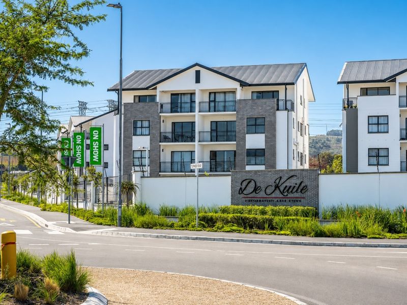 Street view of the De Kuile apartment complex, showcasing modern multi-story residential buildings with balconies and secure perimeter walling.