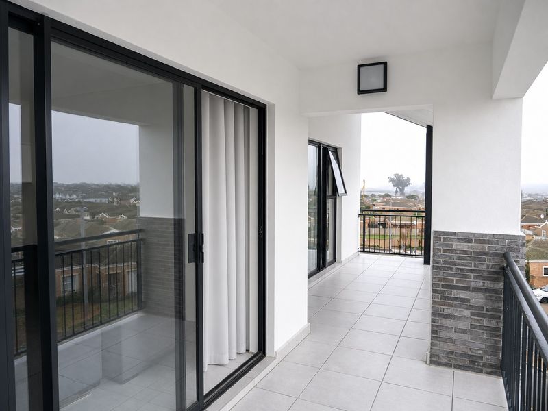 A modern, covered balcony featuring tiled flooring, sleek sliding glass doors, and a metal balustrade with views of the surrounding neighborhood.