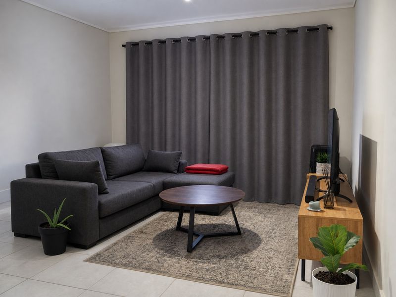 A well-maintained living room featuring neutral tiled flooring and full-length window curtains, providing a clean and functional space.