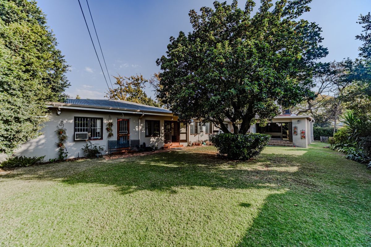 A view of the rear elevation of the house featuring a spacious lawn, mature trees, and a covered patio area.