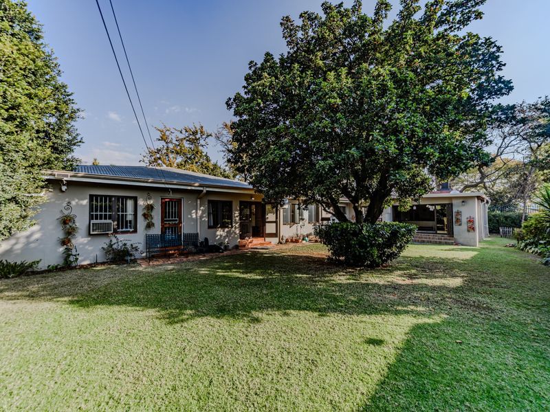 A view of the rear elevation of the house featuring a spacious lawn, mature trees, and a covered patio area.