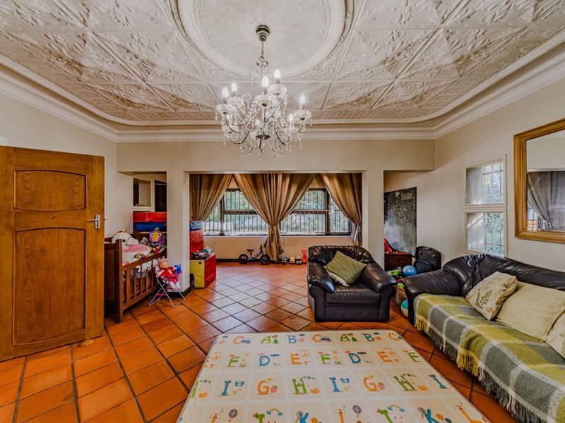 Spacious living room featuring a decorative pressed metal ceiling, crystal chandelier, and classic terracotta floor tiles, offering a character-filled living space.