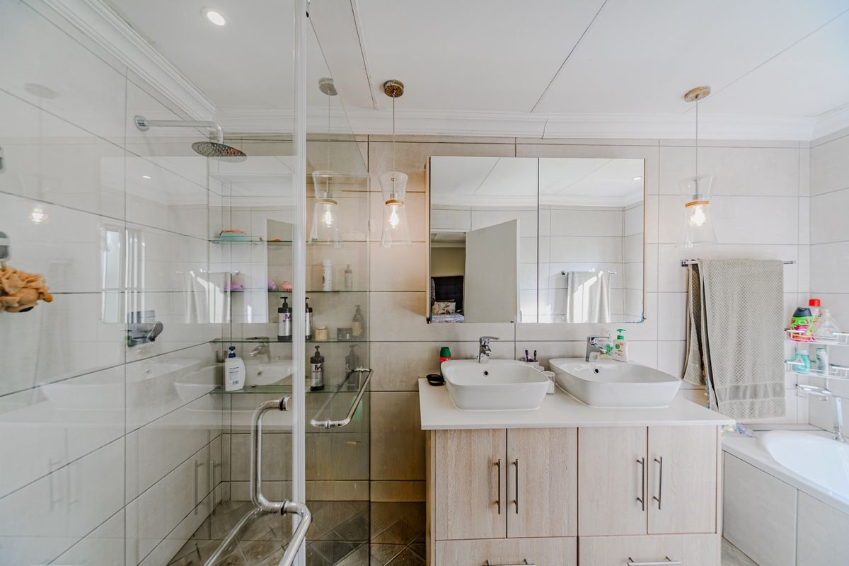 Modern bathroom featuring a double vanity with vessel sinks, a glass-enclosed rain shower, and a built-in bathtub with neutral wall tiling.