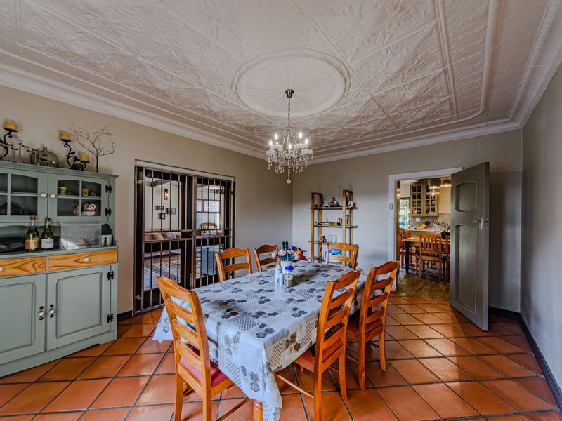 Spacious dining room featuring a classic ornate pressed metal ceiling, terracotta floor tiles, and a central crystal chandelier, with access to adjacent living areas.