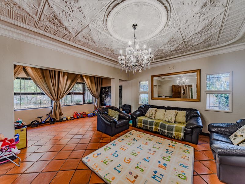 Spacious living room featuring a distinctive ornate pressed metal ceiling, terracotta floor tiles, and a central crystal chandelier.