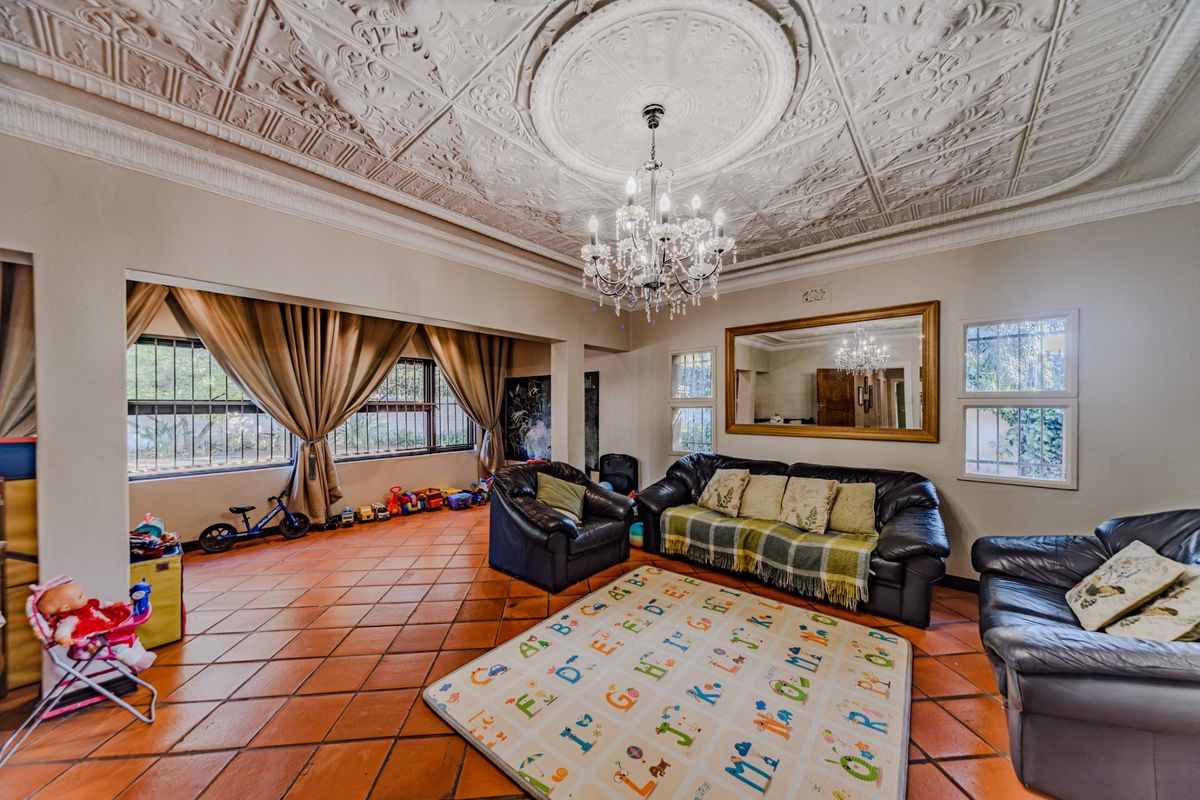 Spacious living room featuring a distinctive ornate pressed metal ceiling, terracotta floor tiles, and a central crystal chandelier.