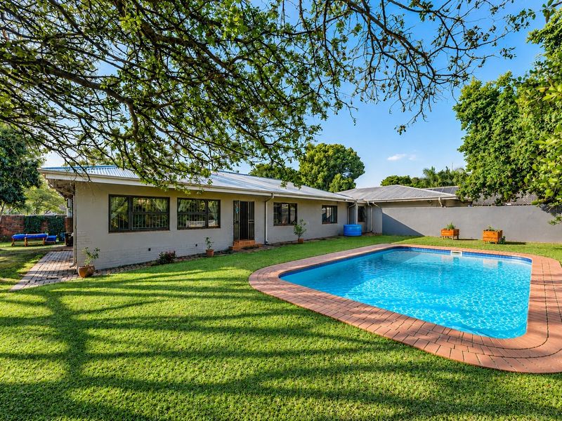 A well-maintained rear garden featuring a swimming pool with brick coping, a paved patio area, and a spacious lawn.