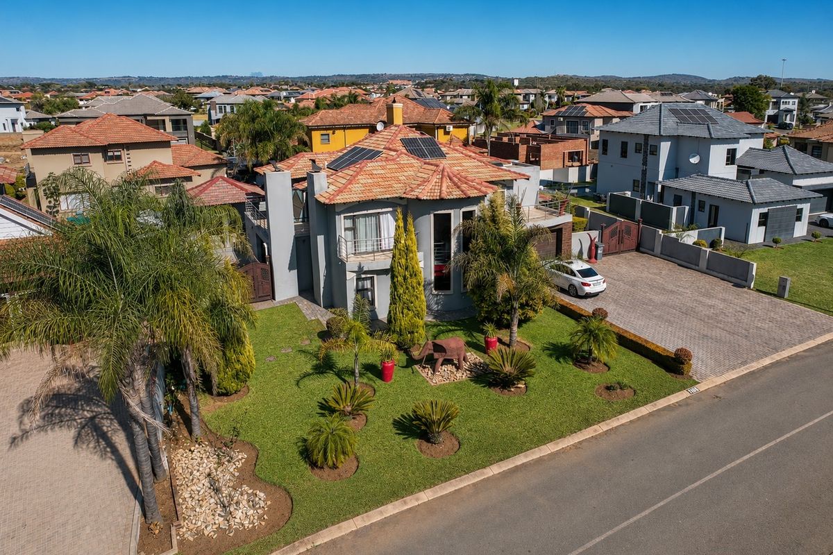 Aerial view of a residential property featuring a tiled roof with solar panels, a paved driveway, and a well-maintained landscaped front garden.
