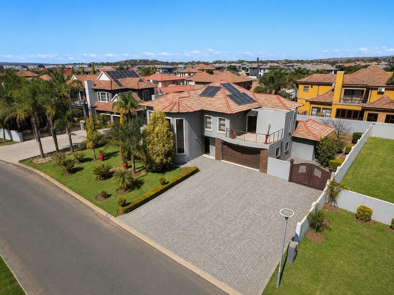 Aerial view of a modern double-story residence featuring a paved driveway, double garage, solar panels, and a well-maintained landscaped garden.