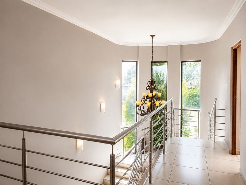 A bright, modern landing area featuring tiled floors, a stainless steel balustrade, and elegant wall lighting with large windows overlooking the garden.