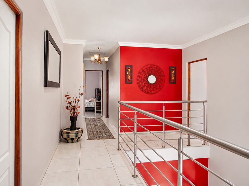 A bright upstairs hallway featuring tiled flooring, a modern stainless steel balustrade, and a bold red accent wall.
