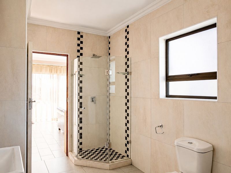 A clean bathroom featuring a glass shower enclosure with decorative checkered tiling, a toilet, and neutral wall tiles.