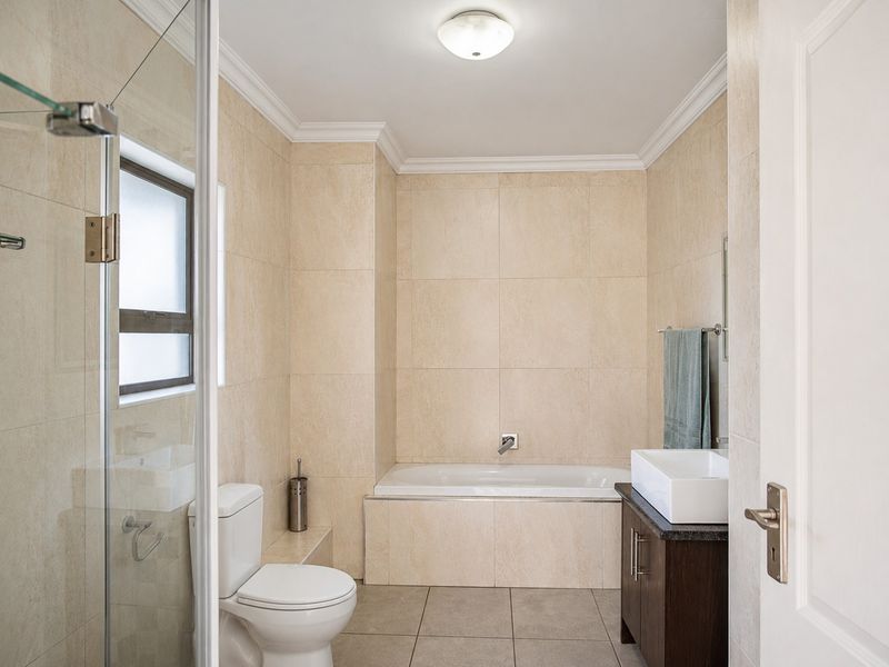 A well-maintained bathroom featuring a built-in bathtub, glass-enclosed shower, modern vanity with basin, and neutral floor-to-ceiling tiling.