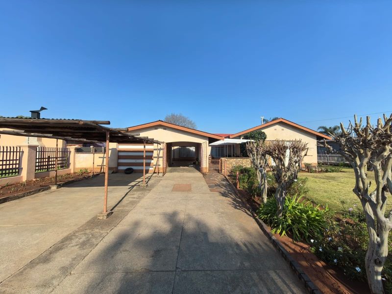 Front view of the property featuring a concrete driveway, attached carport, and established garden area with perimeter fencing.