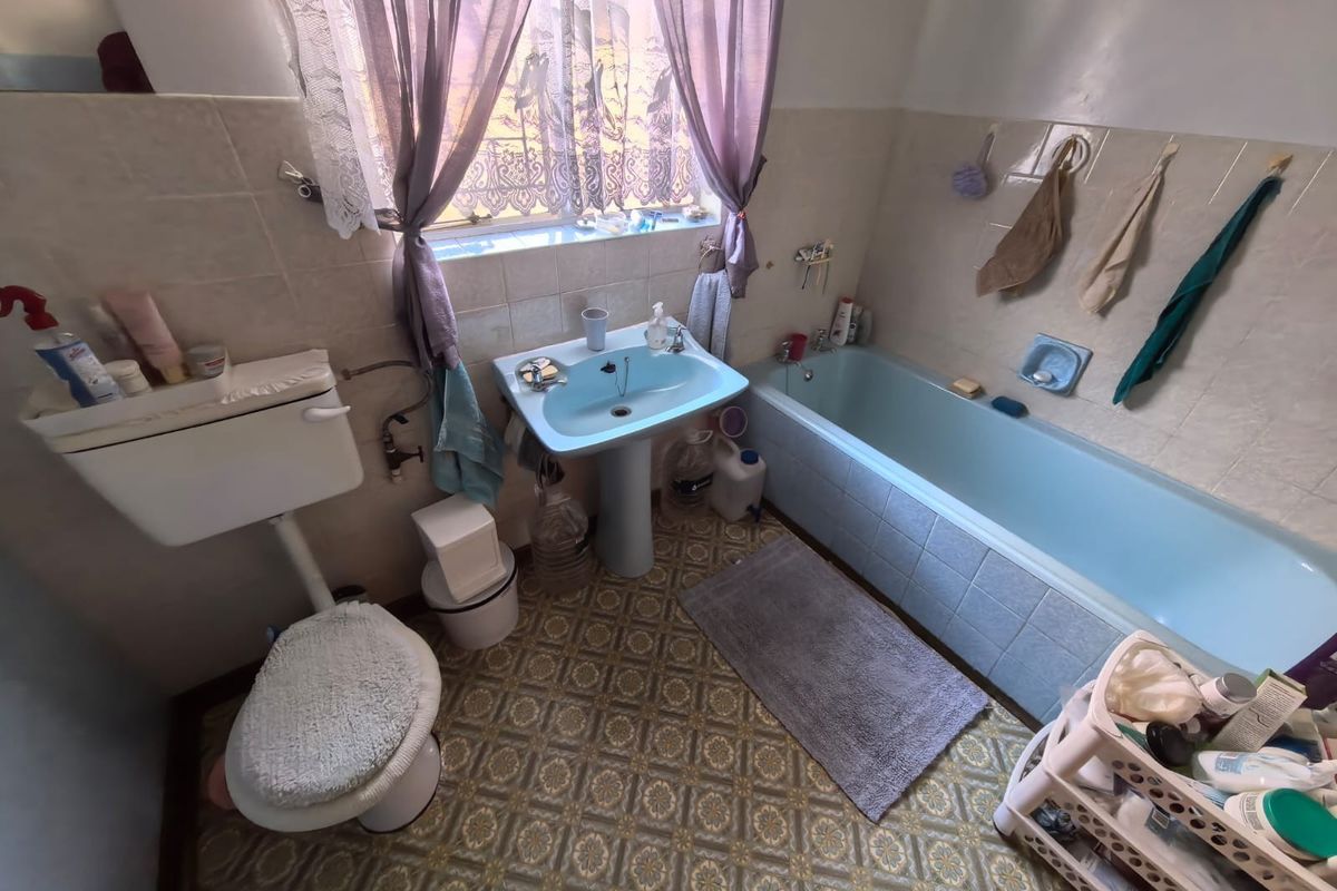 A dated bathroom featuring a blue pedestal basin and matching bathtub, with tiled walls and patterned vinyl flooring.