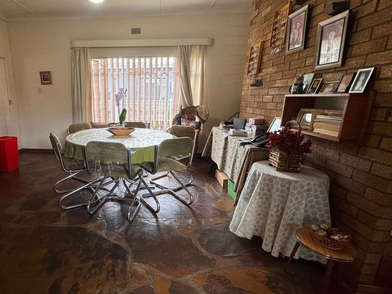Dining room featuring a prominent exposed brick wall and unique natural stone crazy paving flooring, offering a rustic aesthetic with large window for natural light.