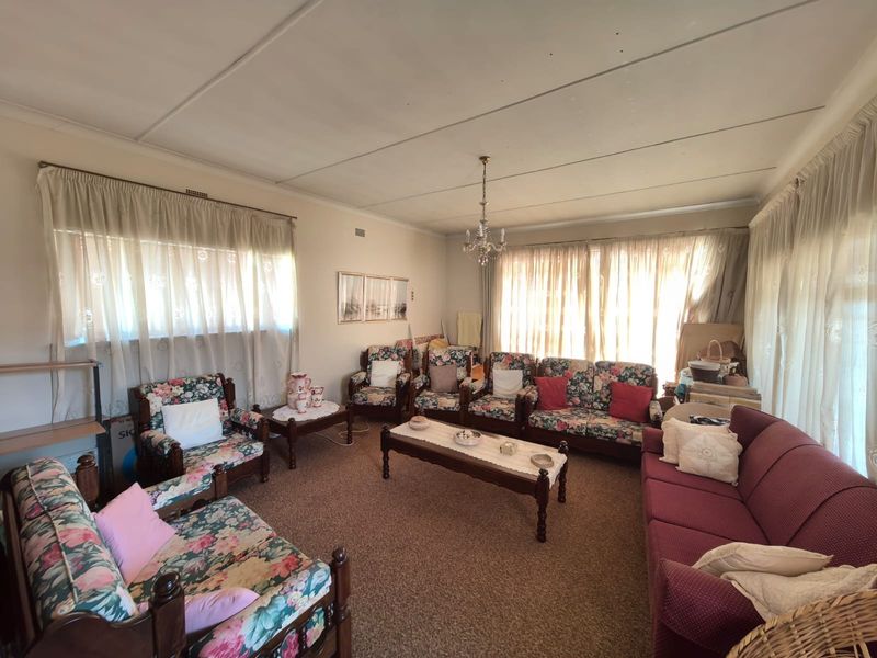 A spacious living room featuring carpeted flooring and a central chandelier, offering a traditional layout with ample natural light from multiple windows.