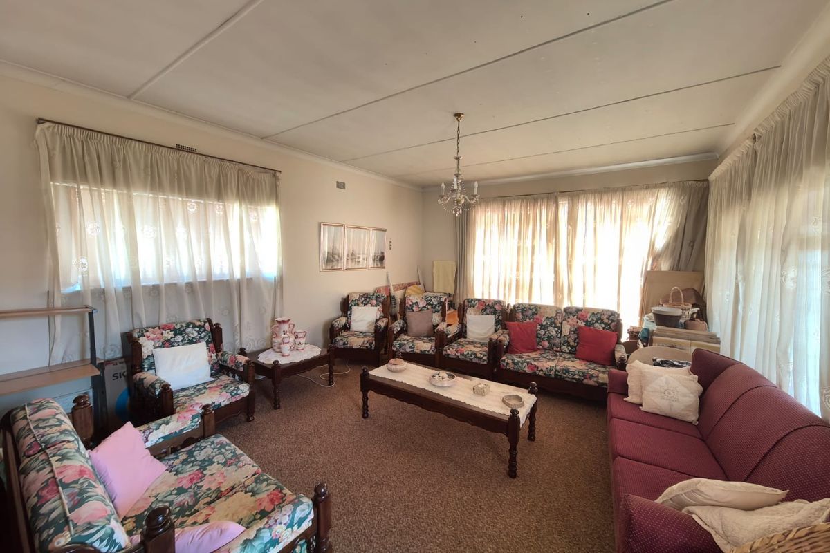 A spacious living room featuring carpeted flooring and a central chandelier, offering a traditional layout with ample natural light from multiple windows.