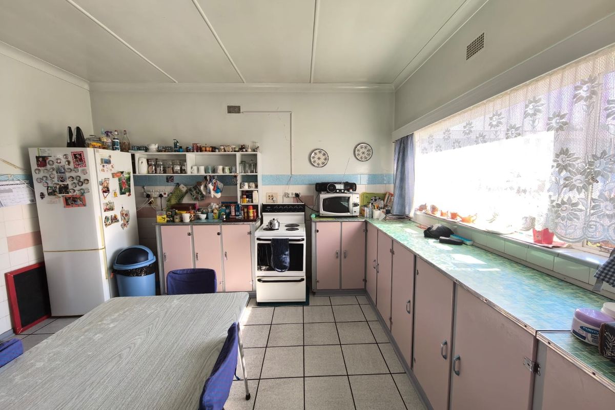 A dated kitchen featuring original cabinetry, tiled flooring, and a large window providing ample natural light, offering significant potential for modernization.