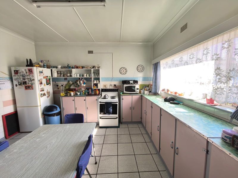 A dated kitchen featuring original cabinetry, tiled flooring, and a large window providing ample natural light, offering significant potential for modernization.
