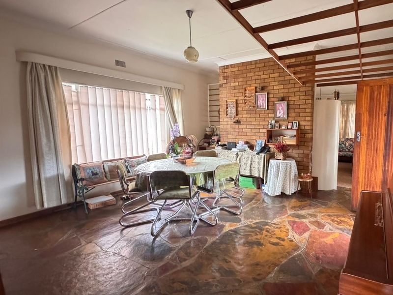 Dining room featuring a rustic exposed brick wall, unique crazy paving stone flooring, and exposed timber ceiling beams, offering a character-filled space.