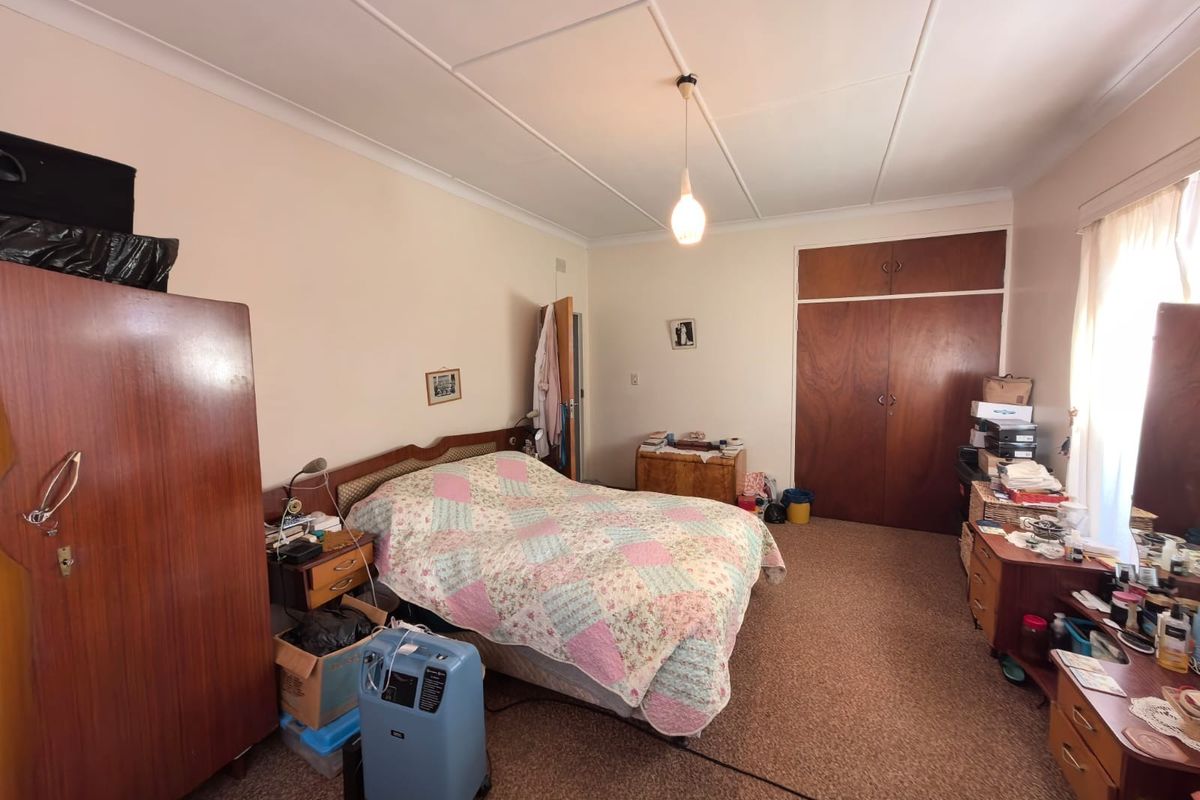 A spacious bedroom featuring built-in wooden cupboards, coved ceilings, and carpeted flooring, offering a functional layout with potential for modernization.