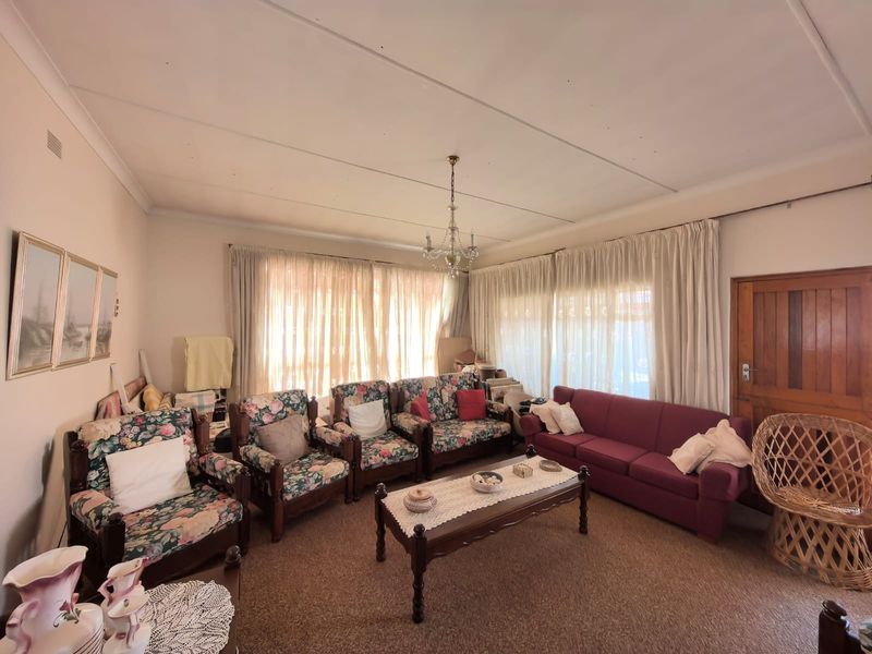 A spacious living room featuring a classic chandelier, timber door, and ceiling cornice, offering a traditional layout ready for modern updates.