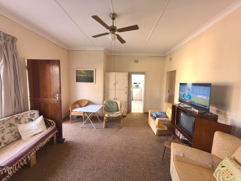 A spacious living room featuring a ceiling fan, built-in storage, and carpeted flooring, offering a functional layout with direct access to the kitchen area.