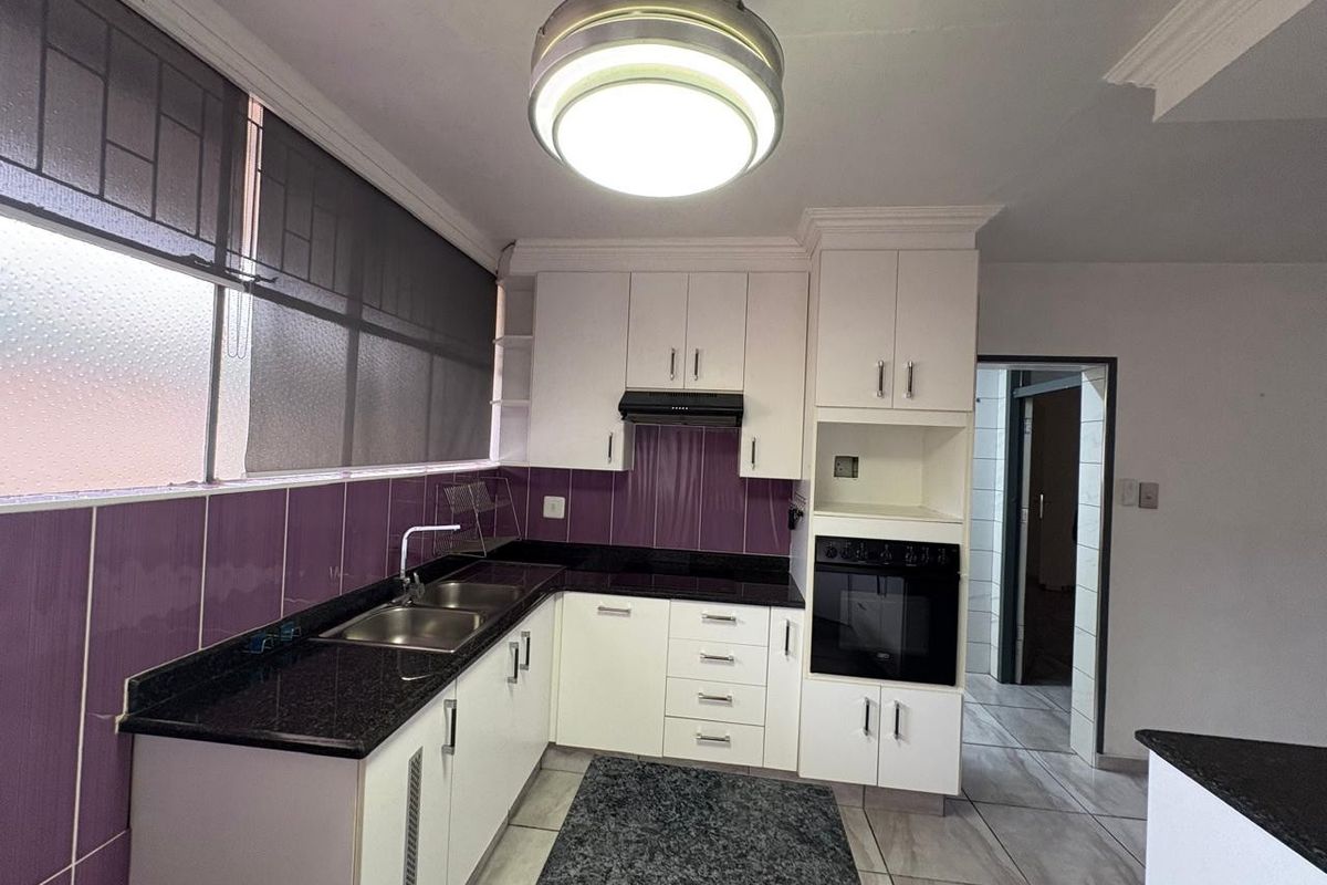 A clean, functional kitchen featuring white cabinetry, dark granite countertops, a built-in oven, and a purple tiled backsplash.