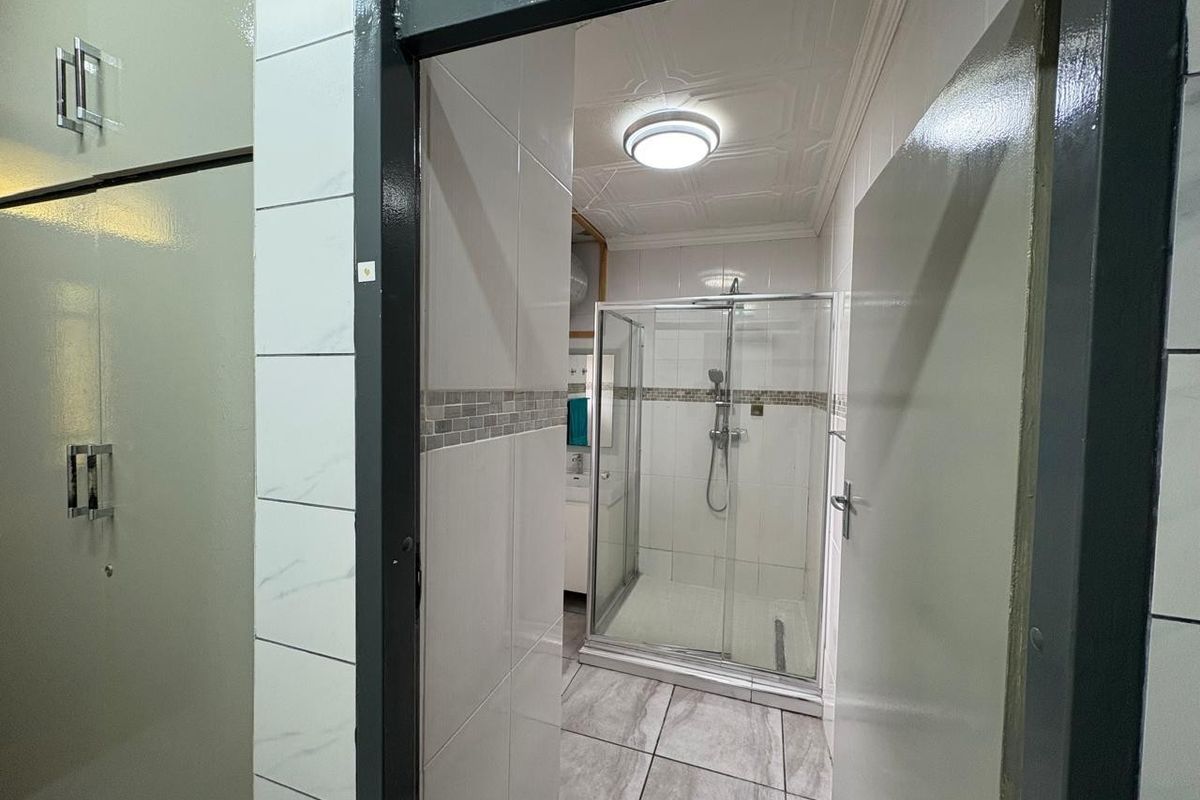 A clean, modern bathroom featuring a glass-enclosed shower, neutral wall and floor tiling, and built-in cabinetry.