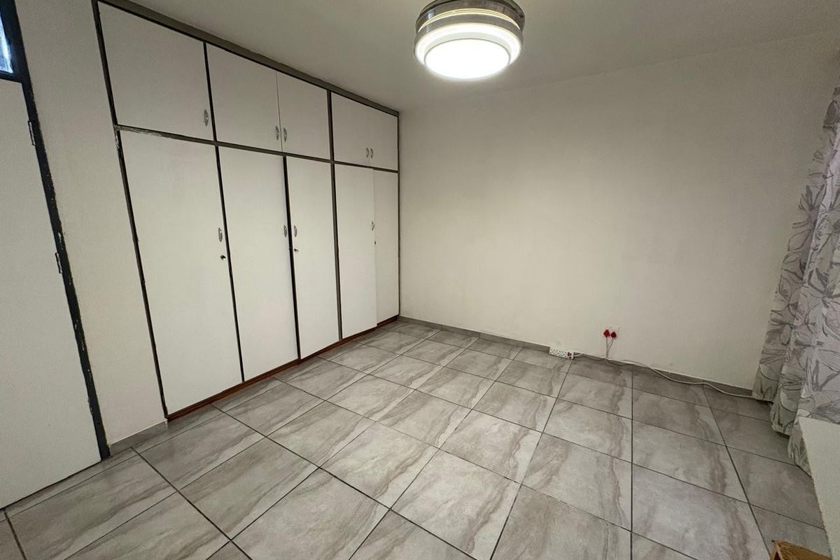 A clean, empty bedroom featuring neutral tiled flooring and extensive built-in cupboard storage, providing a versatile space ready for personalization.