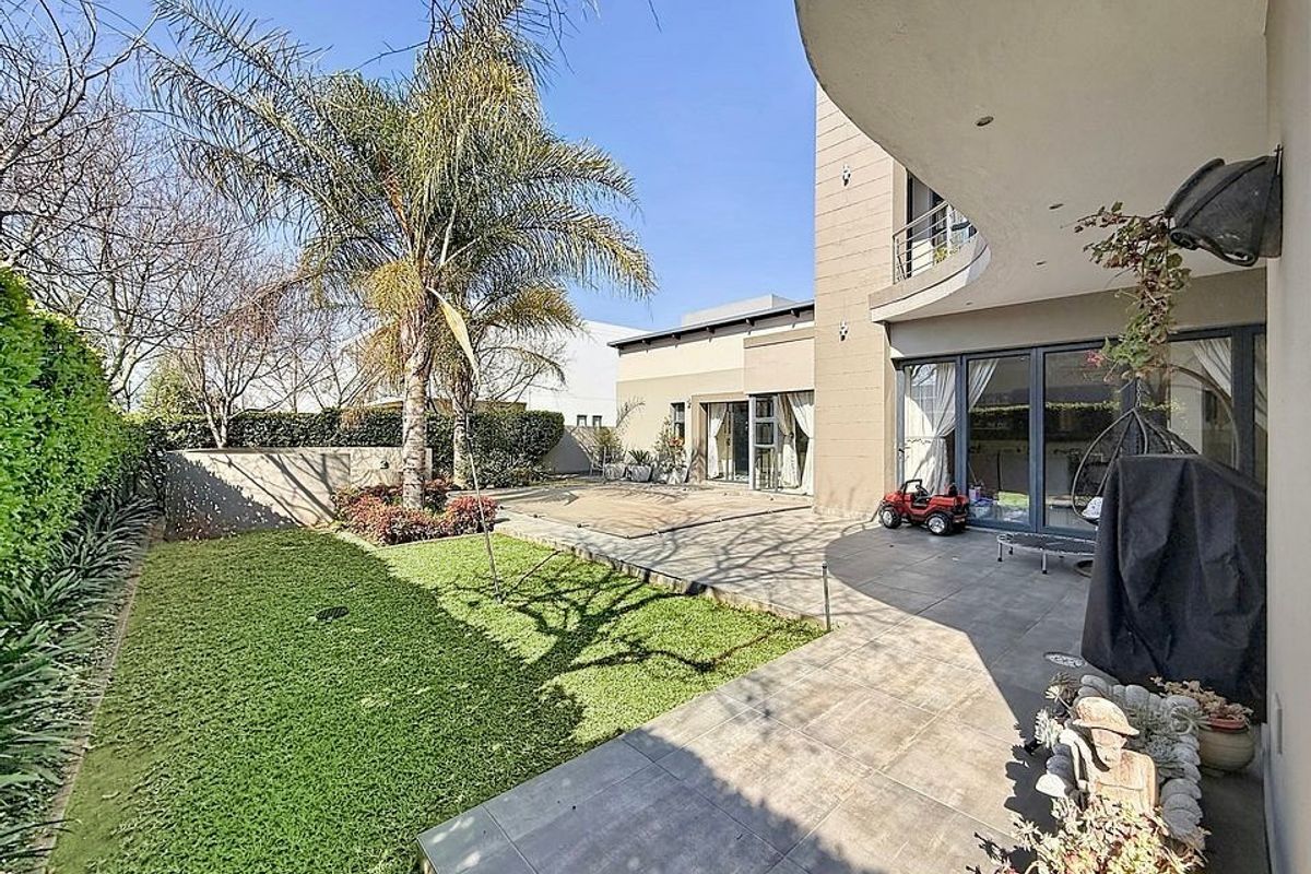 A well-maintained rear garden featuring a tiled patio area, lawn, and access to the home via large sliding glass doors.