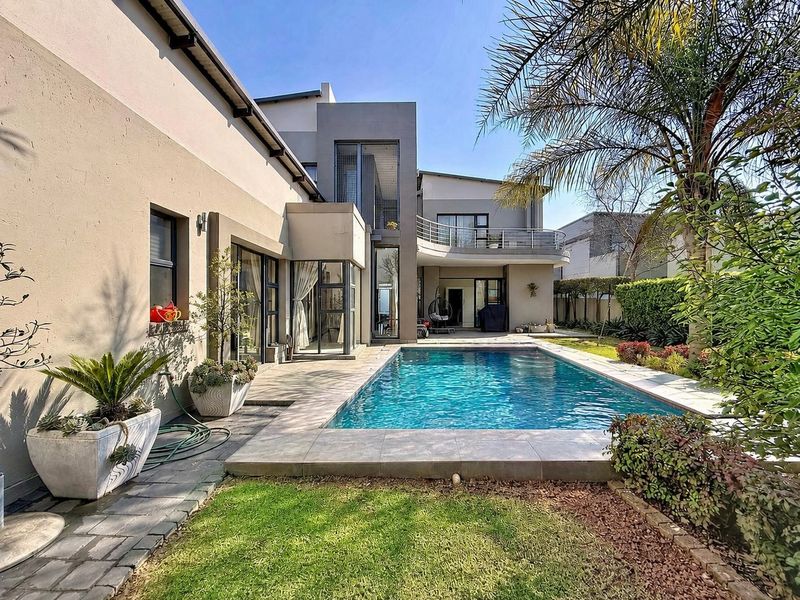 A well-maintained rear exterior view featuring a swimming pool, tiled patio area, landscaped garden, and a modern two-story house facade with a balcony.