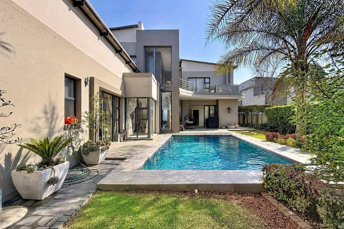 A well-maintained rear exterior view featuring a swimming pool, tiled patio area, landscaped garden, and a modern two-story house facade with a balcony.